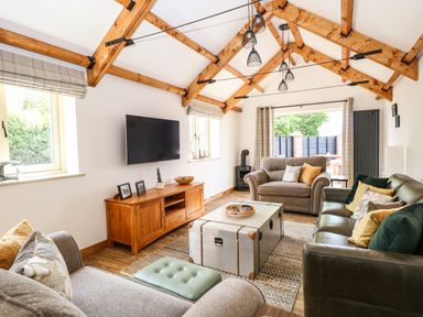A living room with wooden beams on the ceiling a wall-mounted TV sofas a wooden cabinet and a metal trunk coffee table at Cobblers Barn Repps With Bastwick near Potter Heigham