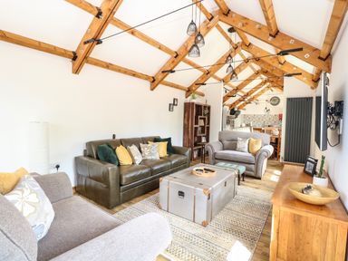 A living room with sofas, a coffee table, wooden beams on the ceiling, and a wooden cabinet at Cobblers Barn in Repps With Bastwick near Potter Heigham