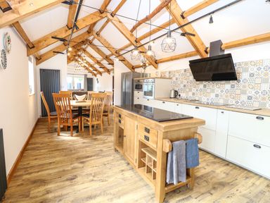 A kitchen with wooden dining table and chairs an island with hanging towels and patterned tile backsplash at Cobblers Barn in Repps With Bastwick near Potter Heigham