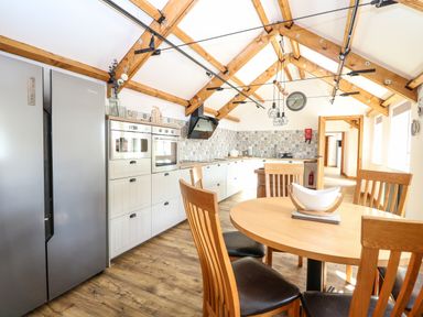 A kitchen with wooden ceiling beams a round dining table wooden chairs and patterned tile backsplash at Cobblers Barn in Repps With Bastwick near Potter Heigham