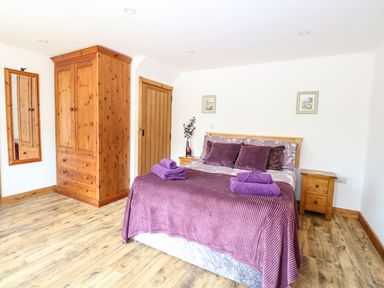 A bedroom with a wooden wardrobe bed with purple bedding and towels at Cobblers Barn in Repps With Bastwick near Potter Heigham