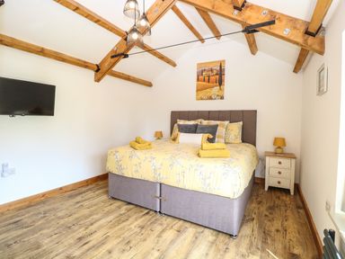A bedroom with a bed and yellow bedding under wooden beams at Cobblers Barn in Repps With Bastwick near Potter Heigham
