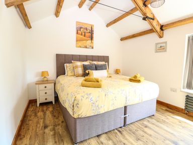 A bedroom with a double bed yellow bedding pillows and towels bedside tables with lamps wooden beams on the ceiling at Cobblers Barn in Repps With Bastwick near Potter Heigham