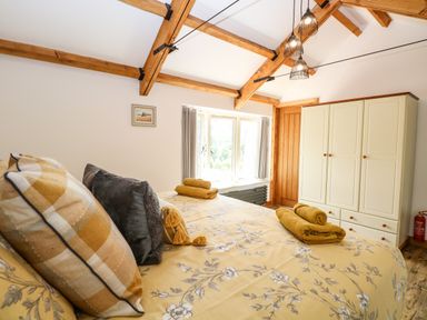 A bedroom with a bed, pillows, towels, a wardrobe, a window, and exposed wooden ceiling beams at Cobblers Barn in Repps With Bastwick near Potter Heigham