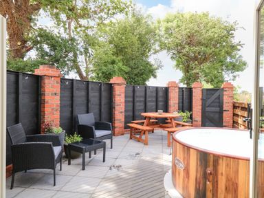 An outdoor patio with black wicker chairs a wooden picnic table and a round wooden hot tub at Cobblers Barn in Repps With Bastwick near Potter Heigham