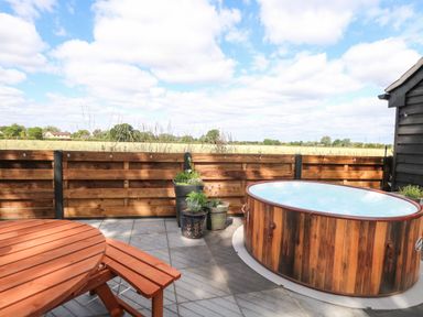 An outdoor patio with a wooden hot tub round table bench and potted plants at Cobblers Barn in Repps With Bastwick near Potter Heigham