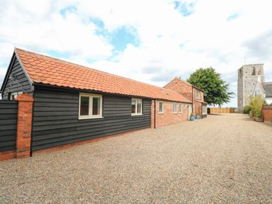 A long building with black and brick walls and a tiled roof on a gravel driveway at Cobblers Barn in Repps With Bastwick near Potter Heigham