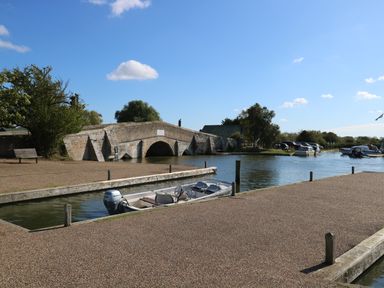 A stone bridge over a river with boats docked by the water at Cobblers Barn in Repps With Bastwick near Potter Heigham