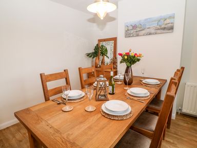 A wooden dining table set for six with plates glasses a bottle and a vase of flowers in a dining room at Cranberry in Bude