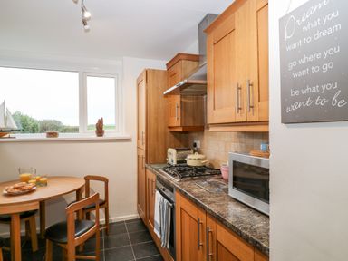 A kitchen with wooden cabinets a round table with chairs and a window at Cranberry in Bude
