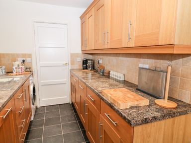 A kitchen with wooden cabinets a white door a coffee maker a toaster a chopping board and a paper towel holder at Cranberry in Bude