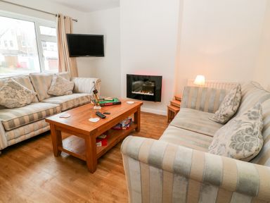 A living room with two striped sofas a wooden coffee table with game boxes and a wall-mounted television at Cranberry in Bude
