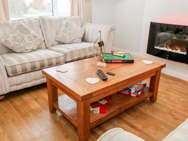 A living room with a striped sofa pillows a wooden coffee table with board games and remote controls and a wall-mounted electric fireplace Cranberry Bude