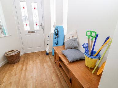 An entrance hall with a wooden bench holding cushions and beach toys next to a white door with patterned glass at Cranberry in Bude