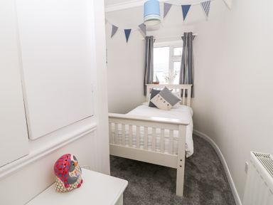 A small bedroom with a single bed a window with curtains a bedside table and bunting on the ceiling at Cranberry in Bude