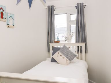 A small bedroom with a single bed white bedding two decorative pillows window with striped curtains decorative sailboat and wall art at Cranberry in Bude