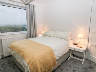A bedroom with a bed covered with white sheets and a yellow blanket next to a window and a nightstand with a lamp at Cranberry in Bude