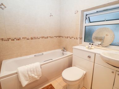 A bathroom with a bathtub toilet sink and a tiled wall at Cranberry in Bude