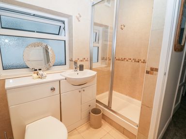 A bathroom with a shower enclosure a toilet a sink with storage cabinets and a round mirror on the window at Cranberry in Bude