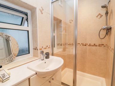 A bathroom with a sink cabinet next to a shower enclosure and a frosted window at Cranberry in Bude