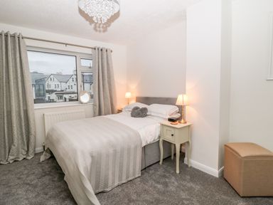 A bedroom with a double bed nightstands with lamps a window with curtains and a small ottoman at Cranberry in Bude