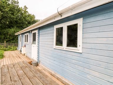 An exterior view of a blue wooden house with white windows and door on a wooden deck at The Beach Shack in Llansteffan