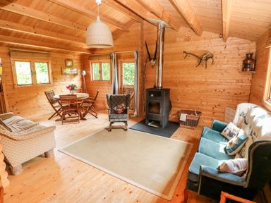 A wooden interior living room with a dining table and chairs a stove armchairs and a sofa at The Beach Shack in Llansteffan