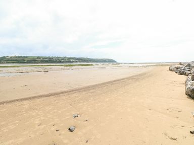 A sandy beach with rocks on the side and hills in the distance at The Beach Shack in Llansteffan