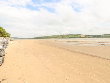 A sandy beach with rocks and grassy hills in the background at The Beach Shack in Llansteffan