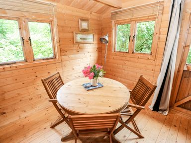 A wooden dining area with a round table and four chairs with flowers on the table at The Beach Shack in Llansteffan