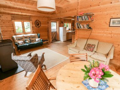 A living room with sofas armchairs a wooden dining table with flowers and a kitchen area at The Beach Shack in Llansteffan