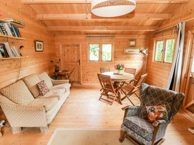 A wooden living room with a sofa a round dining table with chairs and an armchair at The Beach Shack in Llansteffan