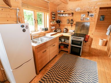 A wooden kitchen with a refrigerator sink stove and open shelves at The Beach Shack in Llansteffan