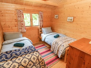 A bedroom with two single beds a striped rug and wooden dresser at The Beach Shack in Llansteffan