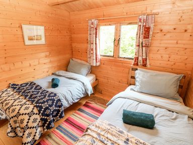 A bedroom with two single beds with blue bedding a window with patterned curtains and a striped rug on the floor at The Beach Shack in Llansteffan