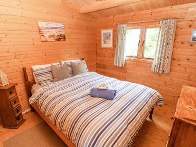 A bedroom with a striped bedspread two windows and wooden furniture at The Beach Shack in Llansteffan