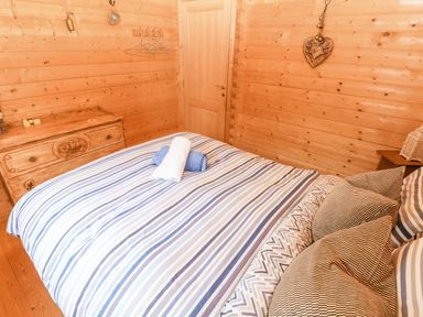 A bedroom with a bed with striped bedding a wooden dresser and wooden walls at The Beach Shack in Llansteffan