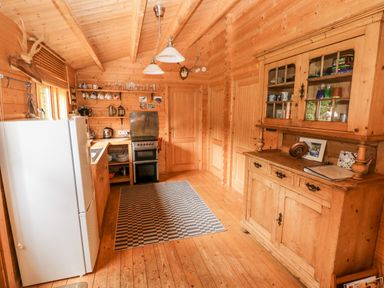 A kitchen with wooden cabinets a refrigerator an oven shelves a rug and a wooden cupboard at The Beach Shack in Llansteffan