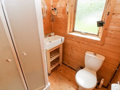 A bathroom with a toilet a sink on a wooden stand a round mirror and a window at The Beach Shack in Llansteffan