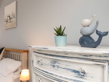 A bedside table with a small plant in a pot and three stacked whale figurines near a bed with a lamp on at The Granary - Rhoscolyn