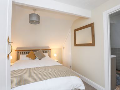 A bedroom with a double bed and cushions bedside lamps and a mirror on the wall at The Granary - Rhoscolyn in Rhoscolyn