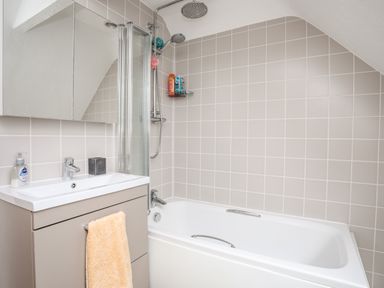 A bathroom with a bathtub shower combination a sink with a cabinet and towel rack at The Granary - Rhoscolyn in Rhoscolyn