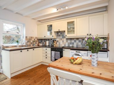 A kitchen with cream cabinets a wooden dining table fruit bowl and flowers at The Granary - Rhoscolyn in Rhoscolyn