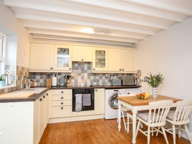 A kitchen with cream cabinets wooden floor a wooden table with chairs and flowers at The Granary - Rhoscolyn in Rhoscolyn