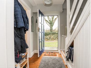 An entry hallway with coats hanging on a rack a shoe rack a blue door open to outside a tree outside and a stairway with a baby gate at The Granary - Rhoscolyn in Rhoscolyn