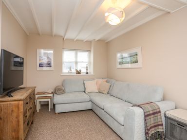 A living room with a light blue sectional sofa a wooden dresser with a tv two framed pictures and a window with blinds at The Granary - Rhoscolyn