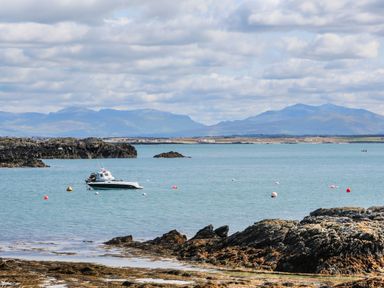 A boat on water near rocky shore with mountains in the background at The Granary - Rhoscolyn