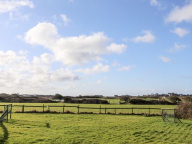 A grassy field with a small fenced soccer area under a partly cloudy sky at The Granary - Rhoscolyn
