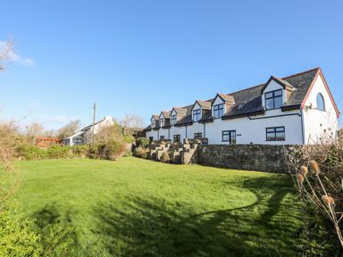 A large white building with multiple dormer windows and a stone wall in front of a grassy yard at The Granary - Rhoscolyn