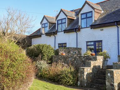 A white house with three dormer windows stone steps and greenery in the garden at The Granary - Rhoscolyn